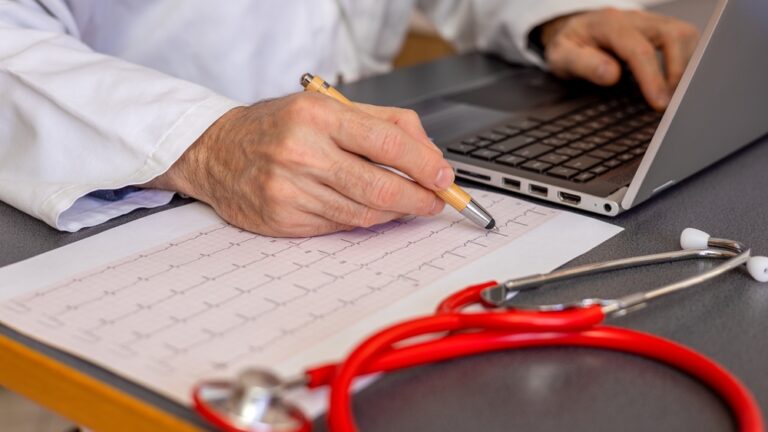 Cardiologist,Doctor,Analyzes,Electrocardiogram,,Office,With,Red,Stethoscope,On,The